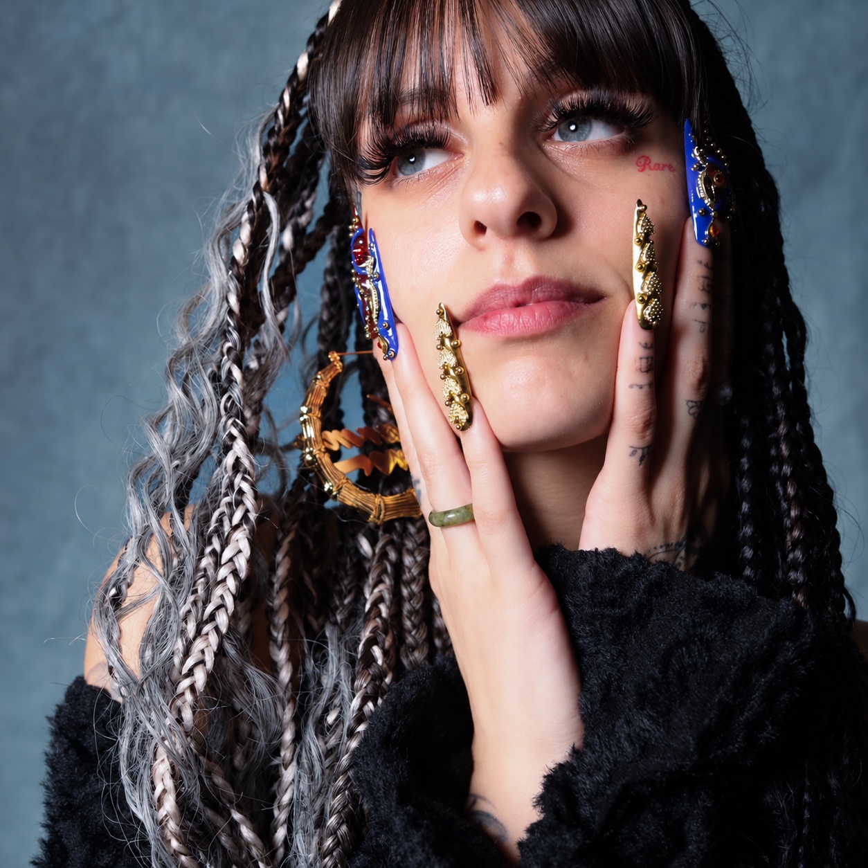 Close-up braided portrait with intricate blue and gold nail art, with AI-assisted photo finishing